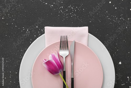 Beautiful table setting with plates,  cutlery, napkin and flower on black background
