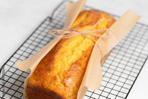 Wallpaper Mural Golden Loaf Cake on Cooling Rack. A freshly baked loaf cake with a warm golden crust rests on a black wire cooling rack, accompanied by a white checkered cloth.  Torontodigital.ca