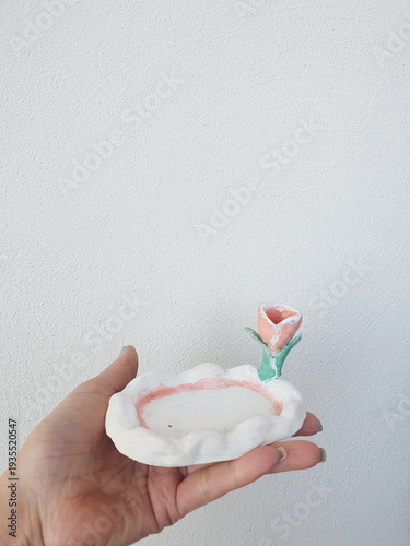 Картината върху платно Hand holding small handmade flower shaped trinket dish with pink rose detail on neutral background