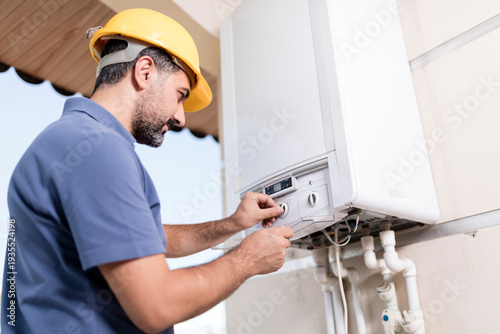 Foto Professional handyman and electrician in blue overalls and yellow safety helmet performing home renovation, repairing boiler and installing electrical wiring in residential interior