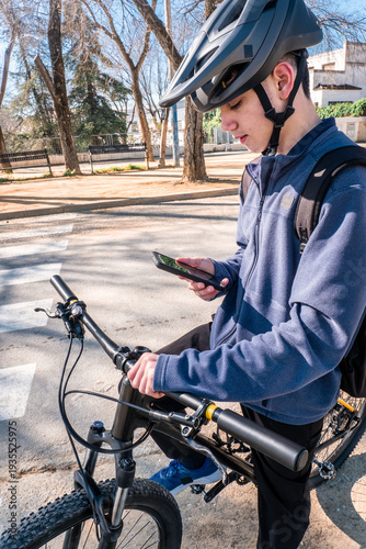 Young male cyclist wearing helmet and backpack, checking directions on his smartphone while standing next to bike
