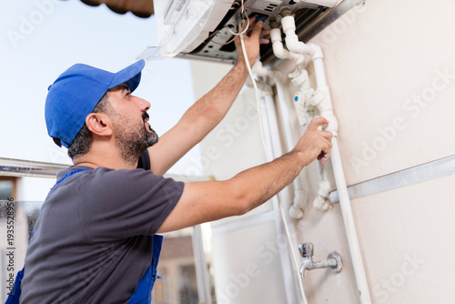 Professional technician in blue uniform and cap inspecting and repairing a domestic gas boiler system.