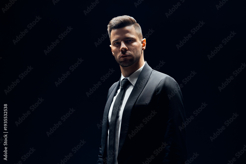 Fototapeta premium Handsome confident man in black suit on dark background