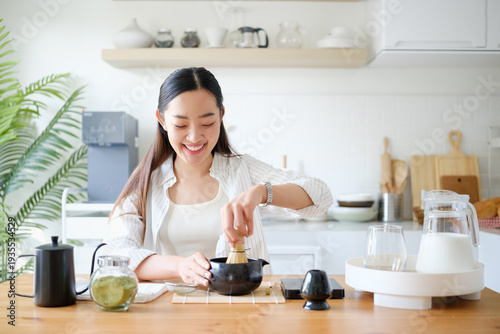 Smiling woman using bamboo whisk to prepare fresh matcha. Healthy lifestyle and wellness drink concept.