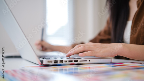 Close up of female designer typing on laptop while using stylus pen in creative workspace. Technology and creativity concept.