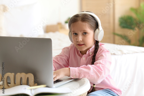 Little girl in headphones with laptop studying computer sciences online at home