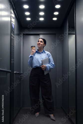 Wallpaper Mural Young professional woman holding coffee cup and laptop inside modern elevator. Concept of busy morning routine, corporate lifestyle and everyday office commute. Torontodigital.ca