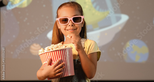 Happy little girl with 3d glasses and popcorn watching cartoons at home