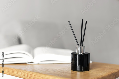 Fotografie Minimalist reed diffuser on wooden shelf with open book, modern home decor concept