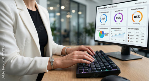 Woman typing on keyboard, reviewing HR analytics dashboard on desktop monitor in a modern office setting