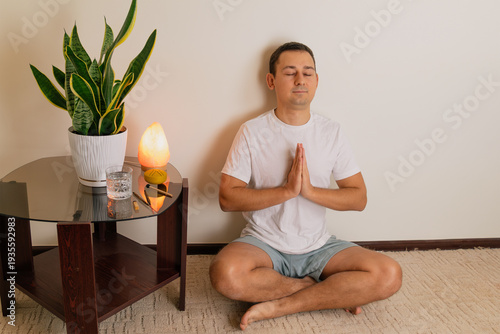 Foto Man meditating cross legged on floor beside side table