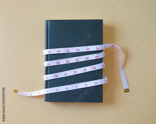 Old book tie around with measuring tape on color background.