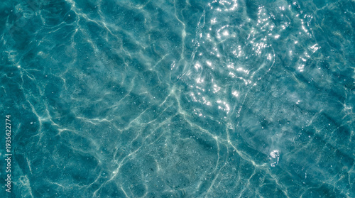 Ultra macro top view of crystal clear azure water with soft ripples and bright sunlight reflections. A serene and fresh texture of a tropical ocean surface, perfect for summer or nature themes.