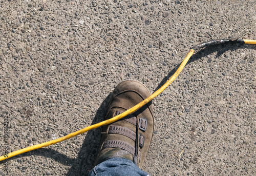 Foot under extension cord. Top view of person almost falling over, stumbling or tripping over power cord. Construction work site safety with power cords. Accident prevention. Selective focus.