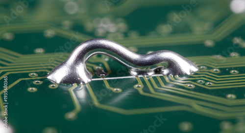 Macro shot of a shiny silver solder joint connecting two points on a green printed circuit board with intricate copper pathways visible