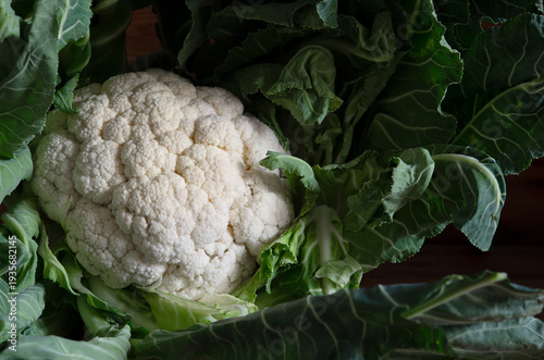 Fresh cauliflower head with green leaves on wood surface