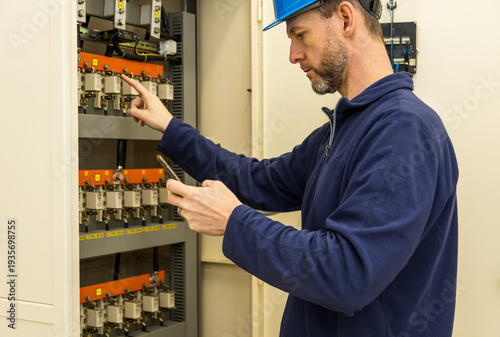 Man, worker in helmet repair, checking circuit breaker with instruction from mobile phone. Self repair maintenance, circuit breaker in electrical substation