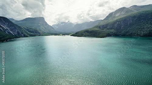 Aerial View of the Eresfjorden and Eresfjord village in Norway under bright hazy cloud sky with steep mountains surrounding the landscape. A view of the turquoise water and the rugged nordic land