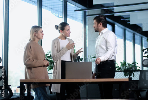 Three people are standing around a desk in a business setting