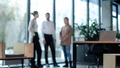 Three people are standing in a room with a potted plant in the background