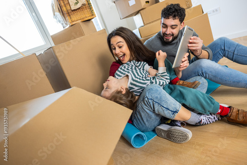 Obraz na płótnie Family bursting into laughter while watching funny videos on a tablet in their new home