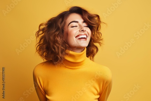 Happy young woman with curly hair wearing a yellow turtleneck laughing cheerfully on a yellow background