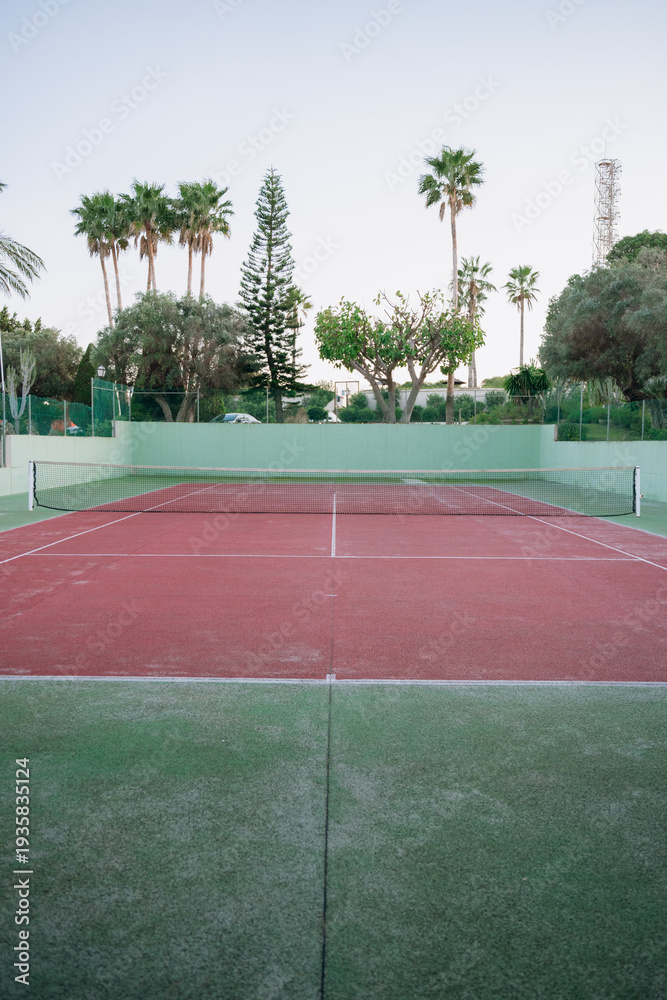 Obraz premium Empty tennis court with red surface and palm trees