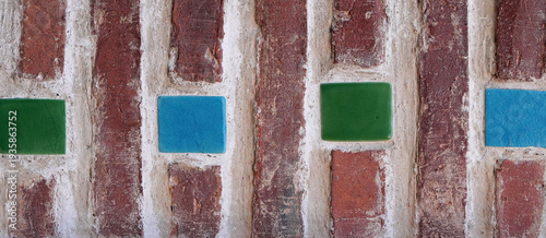 Rustic brick wall texture with embedded green and blue ceramic tiles, showing weathered mortar and architectural decorative detail