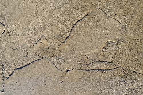 Abstract close-up of a weathered beige plaster wall texture with visible layers, cracks, and rough sandy surface