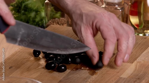 A male chef slices black olives for a salad on a cutting board.