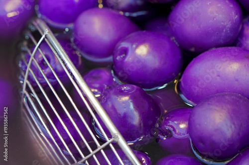 Macro shot of unique vibrant purple olives in brine with a metal spider strainer, showcasing an exotic color variation and glossy food texture