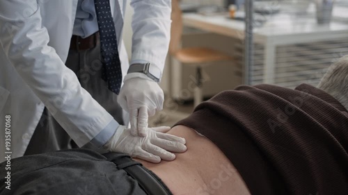 Cropped shot of unrecognizable gloved urologist tapping and palpating patient lower back during physical examination in modern medical office