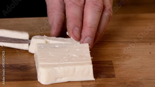 A chef cuts white feta cheese with a knife on a cutting board.
