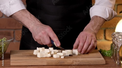 A chef cuts white feta cheese with a knife on a cutting board.