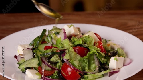 The cook adds vegetable oil dressing to the salad on a white plate.