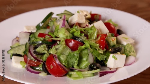 A prepared salad of green lettuce, tomatoes, white feta cheese and black olives swirls on a white plate.