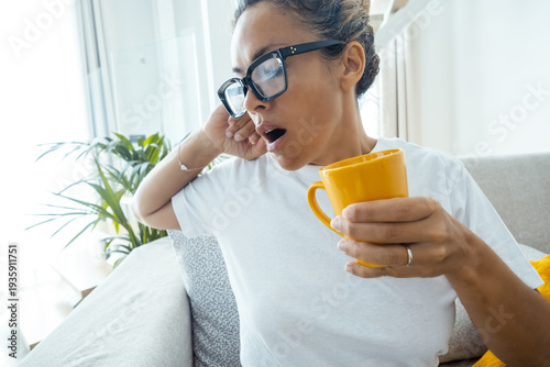 фотографія Tired woman sitting on sofa at home with a cup of tea or coffee yawn ready for a nap or rest time in afternoon leisure activity alone