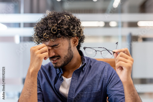 Photography Close-up photo of a tired young Indian man in the office, holding his glasses in