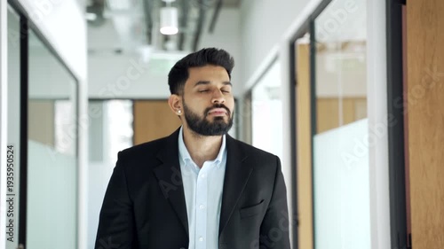 Businessman in formal suit walks along corridor of office building during working day. Confident male manager going to a meeting through modern bright hall of business center, looking away.