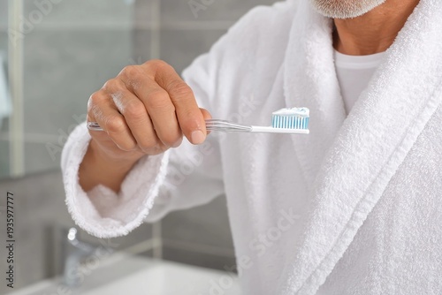 Man brushes teeth in bathroom while wearing white robe in morning routine