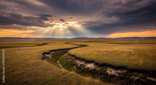 A serene landscape of a winding stream in a vast grassy field at sunset