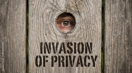 A human eye peeking through a hole in a rustic wooden fence symbolizing the invasion of privacy.