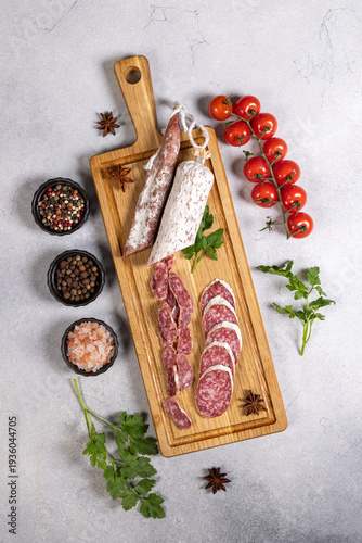 Foto Salami and chorizo on wooden board with spices and tomatoes