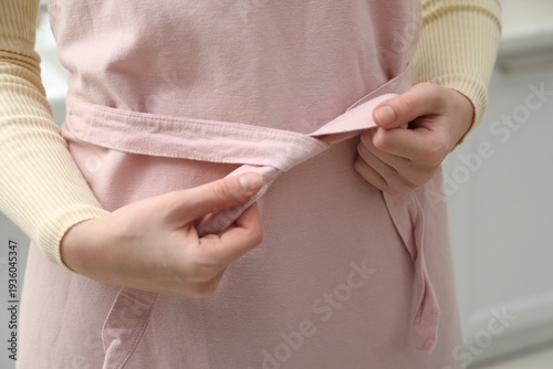 Photos Woman tying clean apron at home, closeup