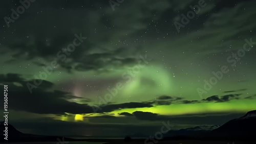 A glowing green aurora borealis dances above dark, silhouetted mountains and still water
