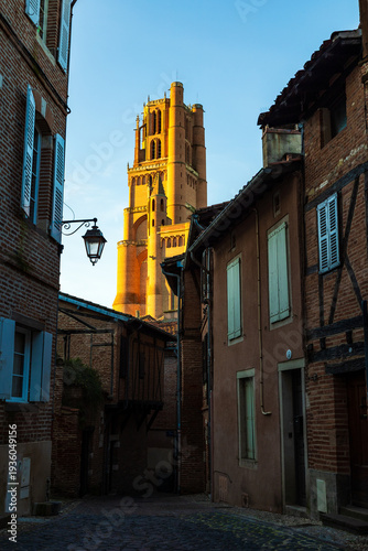 Brick bell tower of Sainte-Cécile Cathedral illuminated by sunset seen from a narrow street in Albi city center