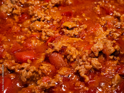 Close-up of minced beef simmering in rich tomato sauce, creating a hearty homemade bolognese. Hot, flavorful meat sauce bubbling in a pan during the cooking process.