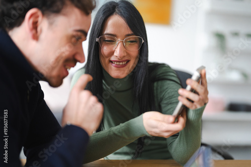 A man and a woman are looking at a smartphone together, sharing a moment of connection and amusement.