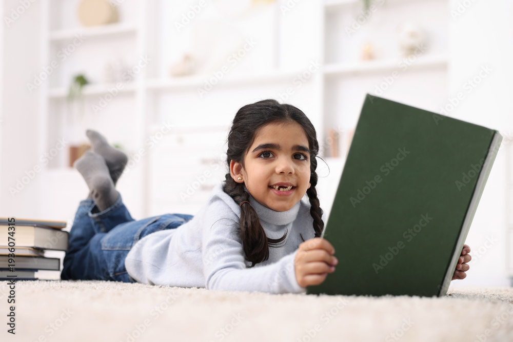 Naklejka premium Cute little girl reading book on floor at home