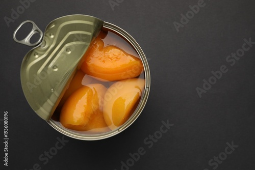 Pickled peaches in tin can on black background, top view. Space for text
